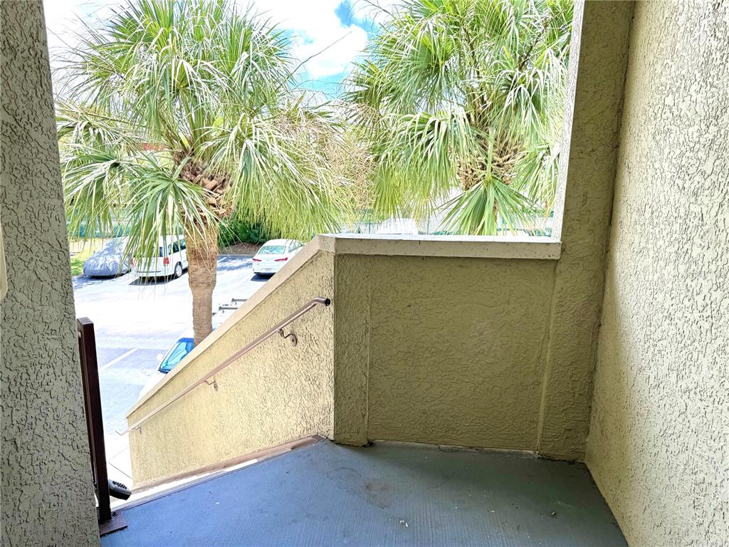 An outdoor stairwell with a metal handrail leads down to a parking lot with palm trees — 1238 S MISSOURI AVENUE UNIT 102, CLEARWATER, FL