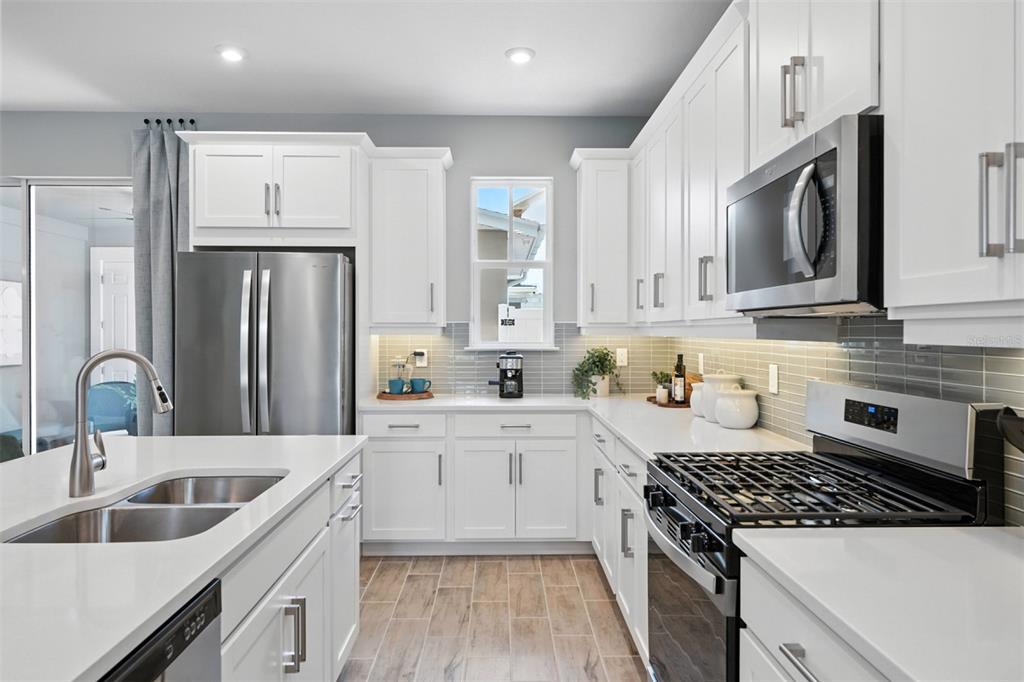 A modern kitchen features white cabinets, stainless steel appliances, quartz countertops, and a tile backsplash — 1792 HEADLAND LOOP, CELEBRATION, FL