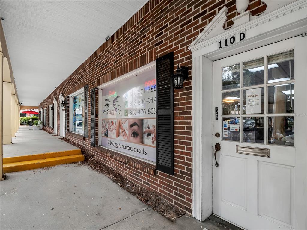 A brick storefront exterior features a white door labeled 110 D and a large window advertisement — 110 LITHIA PINECREST ROAD UNIT D, BRANDON, FL