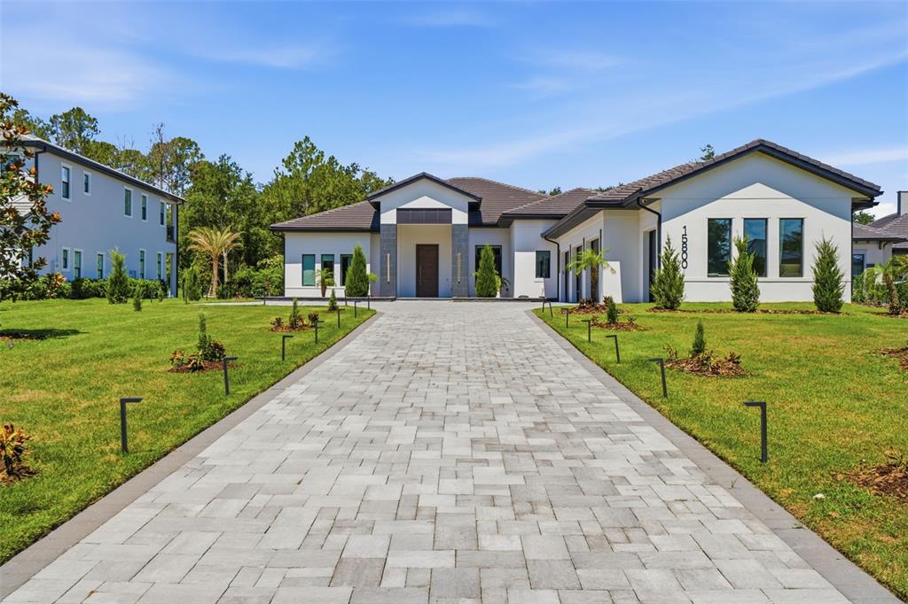 A modern single-story house with a paved driveway and a dark tiled roof — 15800 PENDIO DRIVE, BELLA COLLINA, FL