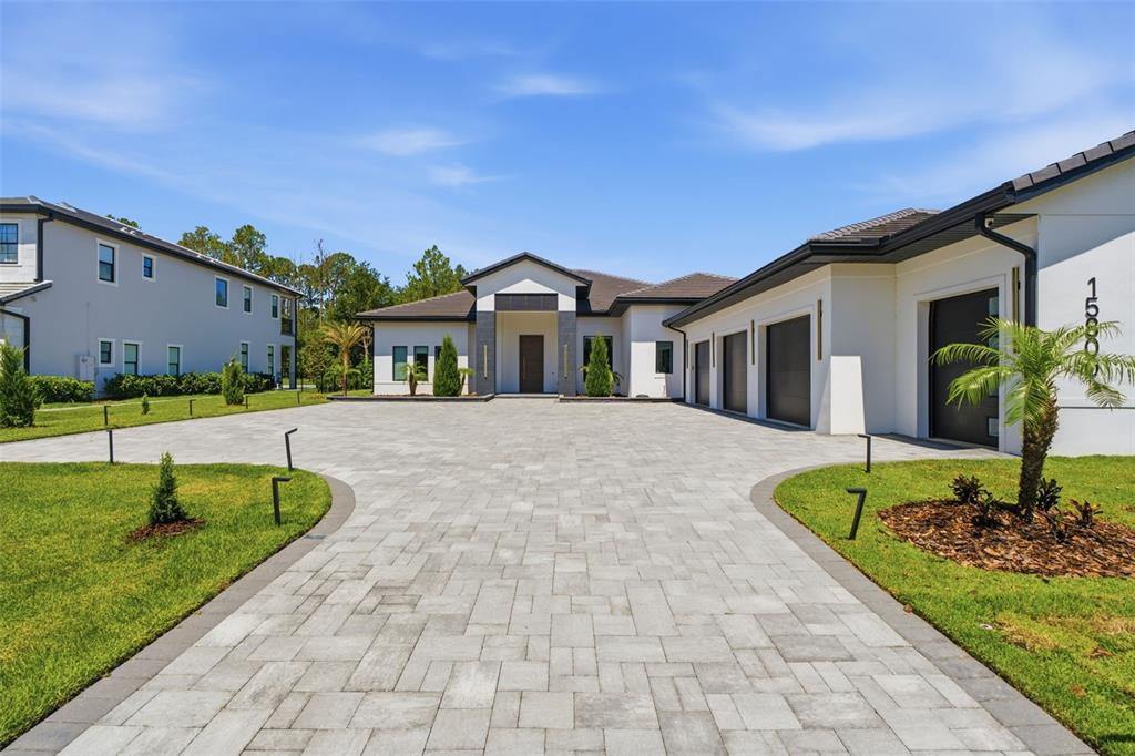 A modern single-story house features a large paved driveway, three garage bays, and white siding — 15800 PENDIO DRIVE, BELLA COLLINA, FL