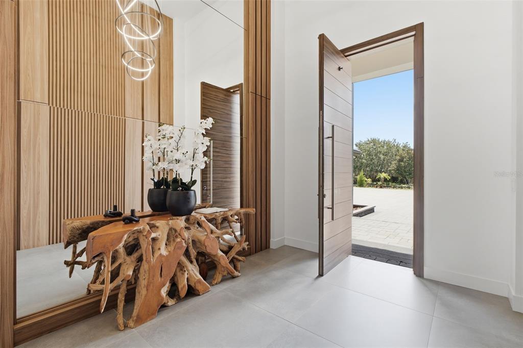 A modern entryway features a live-edge wood console table, white orchids, and a large door — 15800 PENDIO DRIVE, BELLA COLLINA, FL