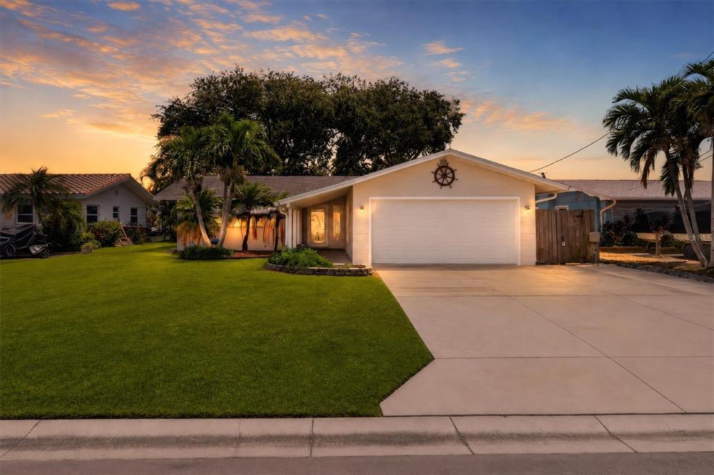 A single-story house with a white garage, a green lawn, and palm trees at sunset — 541 LILLIAN DRIVE, MADEIRA BEACH, FL