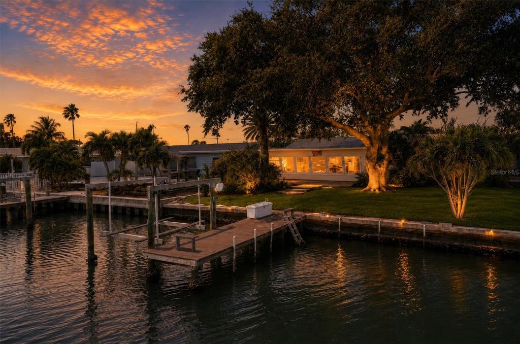 A waterfront house with a wooden dock and boat lift at sunset — 541 LILLIAN DRIVE, MADEIRA BEACH, FL