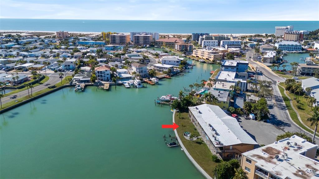 An aerial view shows a waterfront apartment building with a grassy yard and boat docks — 275 116TH AVENUE, TREASURE ISLAND, FL