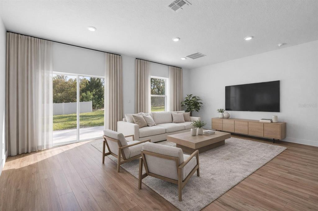 A bright living room features light wood flooring, a large sofa, two chairs, and sliding doors — 4411 SW 172ND STREET ROAD, OCALA, FL