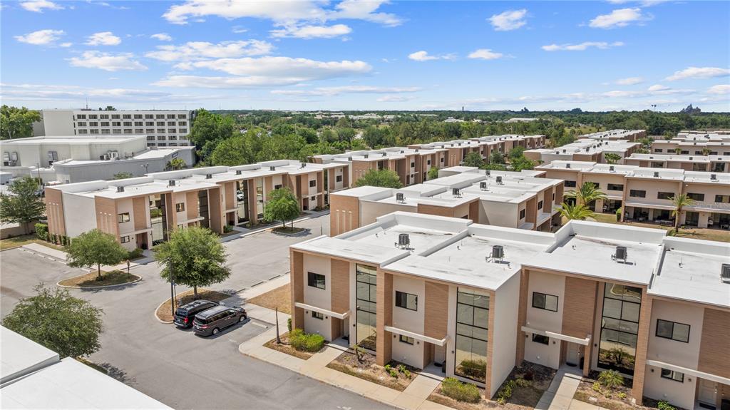 An aerial view shows a complex of modern, multi-story townhomes with flat roofs and parking — 7526 BROOKLYN DRIVE, KISSIMMEE, FL