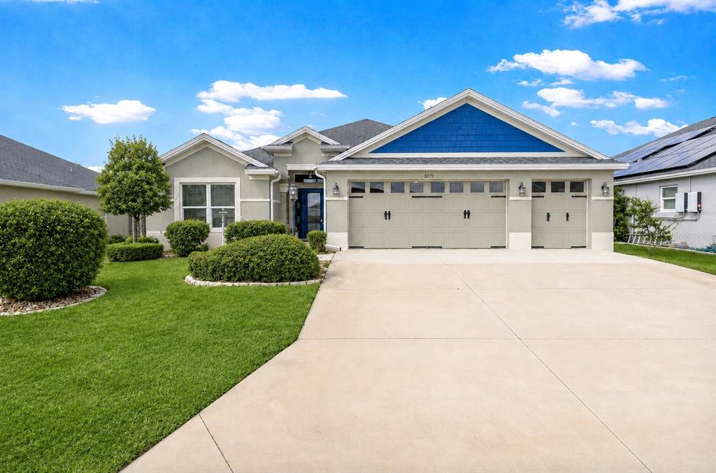 A single-story suburban house features a three-car garage, light stucco walls, and blue siding — 1078 MAYNARD PATH, THE VILLAGES, FL