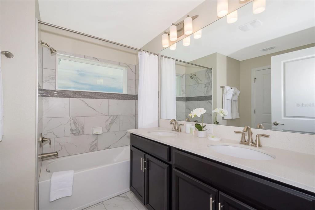 A bathroom with a double vanity, dark cabinets, and a shower-tub combination with marble tile — 8987 BACKSWING WAY, DAVENPORT, FL