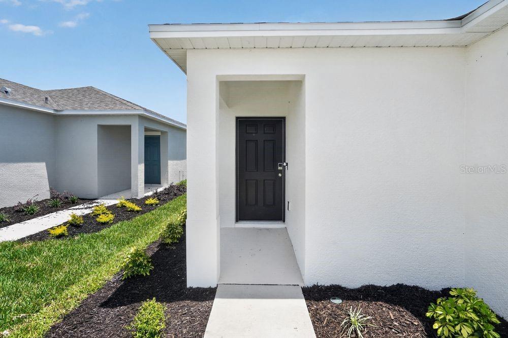 A concrete walkway leads to the dark front door of a white stucco house — 13513 SAWMILL STREET, PARRISH, FL