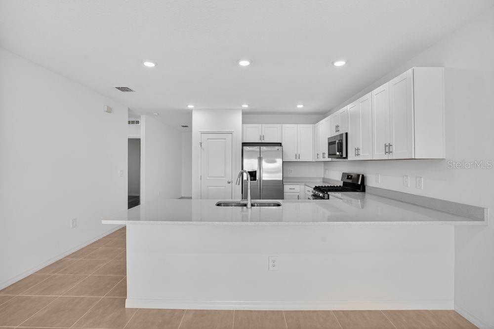 A modern kitchen features white cabinets, stainless steel appliances, and a large quartz-topped island — 13513 SAWMILL STREET, PARRISH, FL