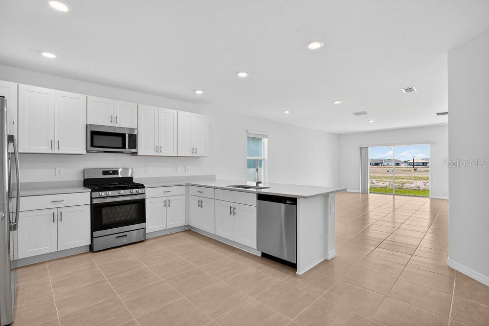 A kitchen with white cabinets, stainless steel appliances, and tile flooring opens to a living area — 13513 SAWMILL STREET, PARRISH, FL