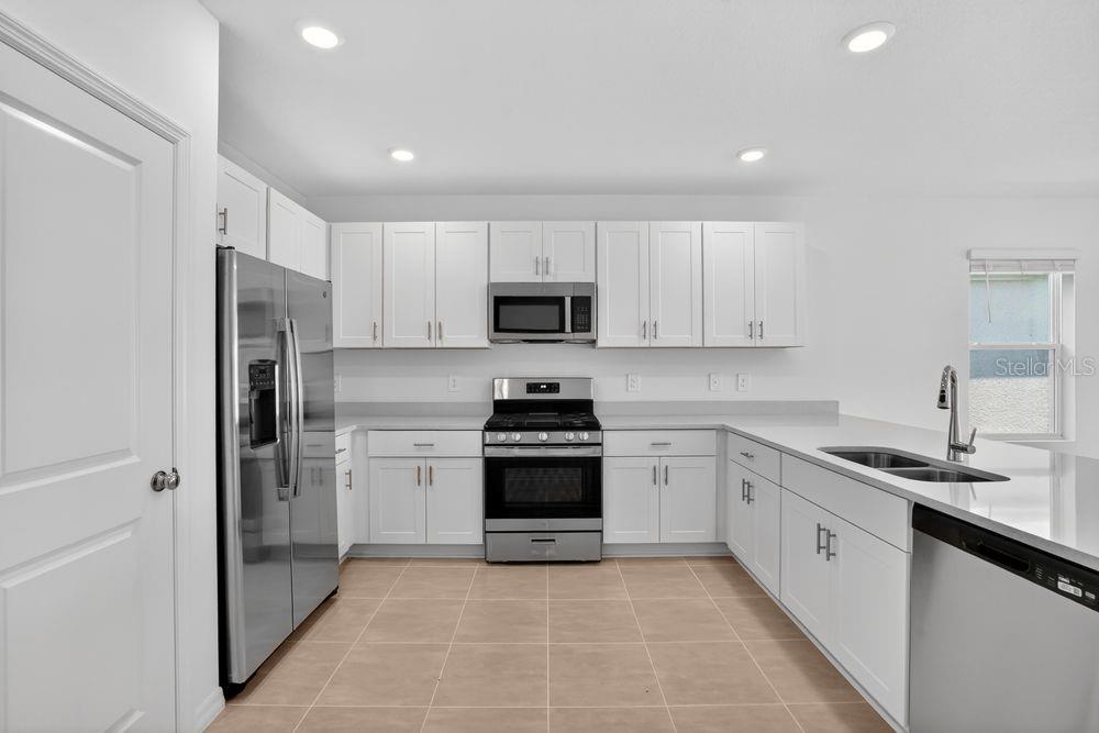 A kitchen with white cabinets, stainless steel appliances, and light-colored tile flooring — 13513 SAWMILL STREET, PARRISH, FL