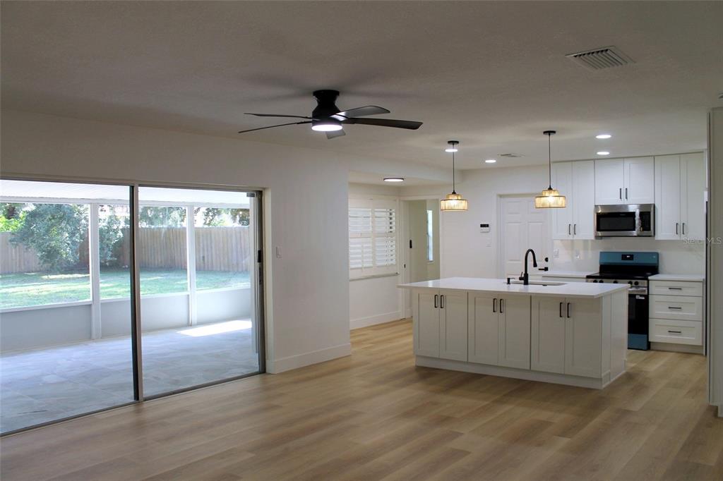 A bright kitchen with a white island and cabinets opens to a living area and patio — 13808 CHERRY BROOK LANE, TAMPA, FL