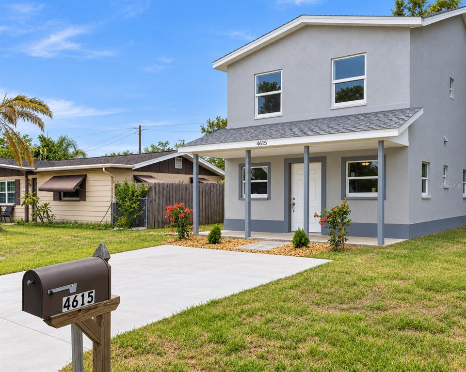 A two-story gray house with a front porch and a concrete driveway stands on grass — 4615 AEGEAN AVENUE, HOLIDAY, FL
