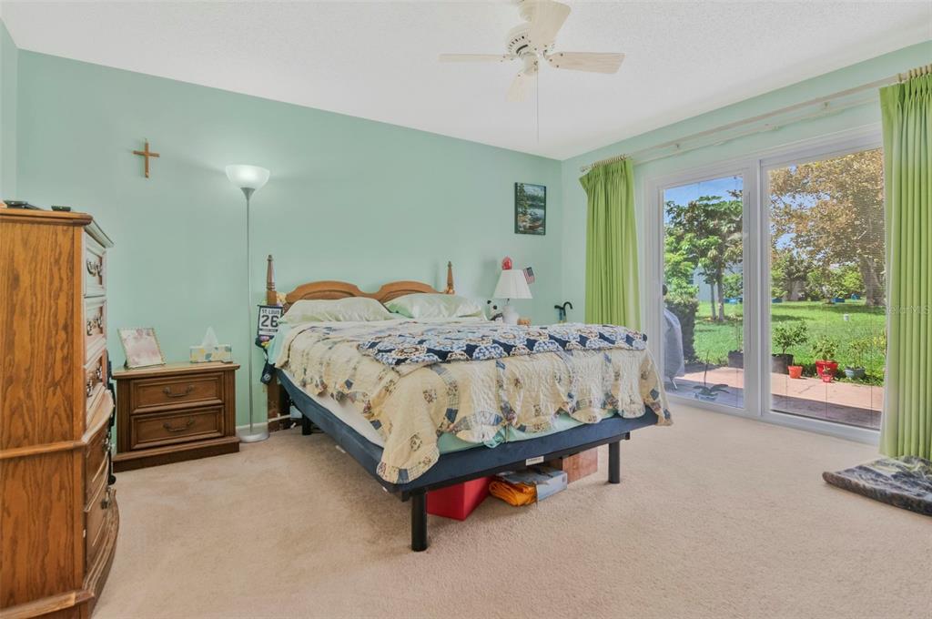 A bedroom with light green walls, a wooden bed frame, and sliding glass doors to a yard — 4111 105TH AVENUE N, CLEARWATER, FL