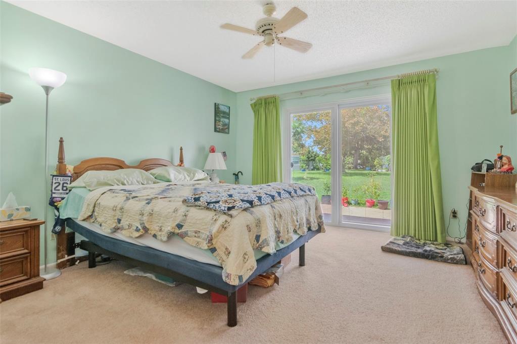 A bedroom with light green walls, a queen bed, carpeted floors, and sliding glass patio doors — 4111 105TH AVENUE N, CLEARWATER, FL