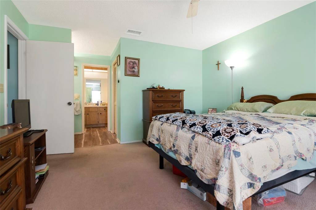 A bedroom with light green walls, a bed, a wooden dresser, and an attached bathroom — 4111 105TH AVENUE N, CLEARWATER, FL