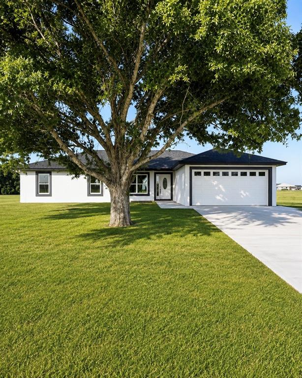 A white single-story house with a large tree in the front yard and a garage — 7016 GOLF CLUB DRIVE, SEBRING, FL