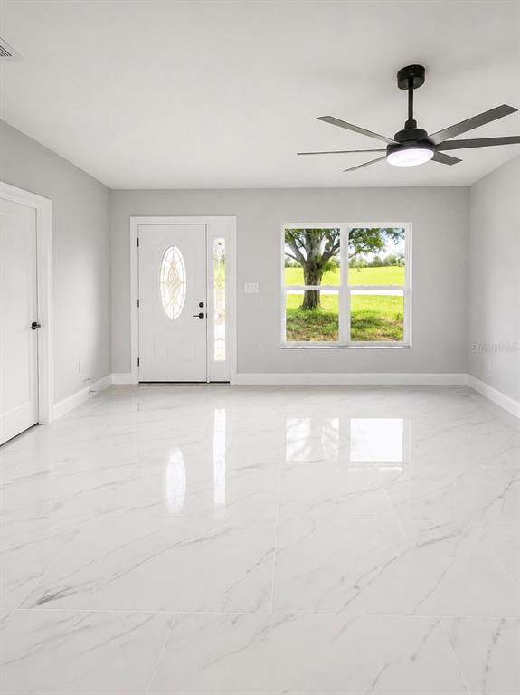 A bright room features white marble-look tile flooring, a ceiling fan, and a front entry door — 7016 GOLF CLUB DRIVE, SEBRING, FL