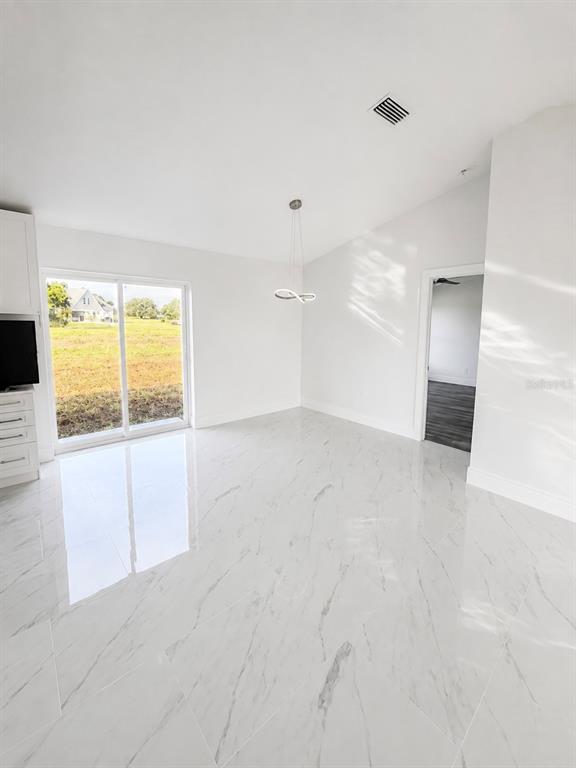 A bright room features white marble-look tile flooring, a modern pendant light, and sliding glass doors — 7016 GOLF CLUB DRIVE, SEBRING, FL