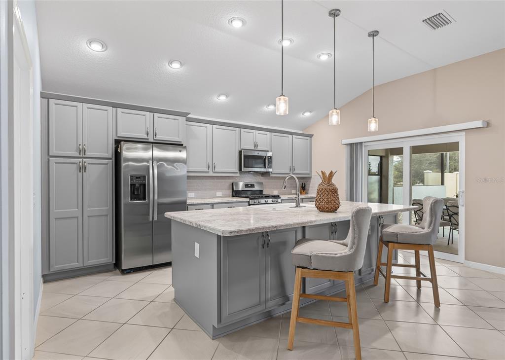 A kitchen with gray cabinets, a large island with bar stools, and stainless steel appliances — 3146 JACQUELINE WAY, THE VILLAGES, FL
