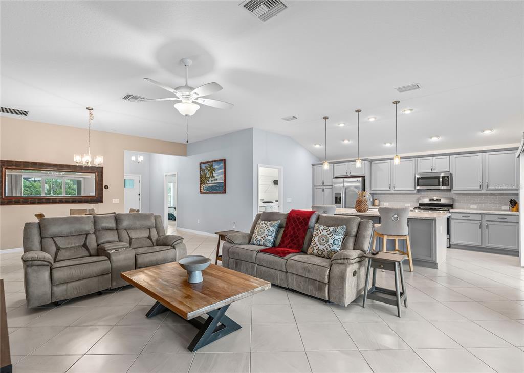 An open-concept living room and kitchen featuring gray sofas, a wooden coffee table, and cabinetry — 3146 JACQUELINE WAY, THE VILLAGES, FL