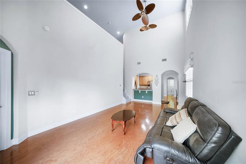 A living room with high ceilings, hardwood floors, a dark leather sofa, and an arched entryway — 4961 ANNISTON CIRCLE, TAMPA, FL