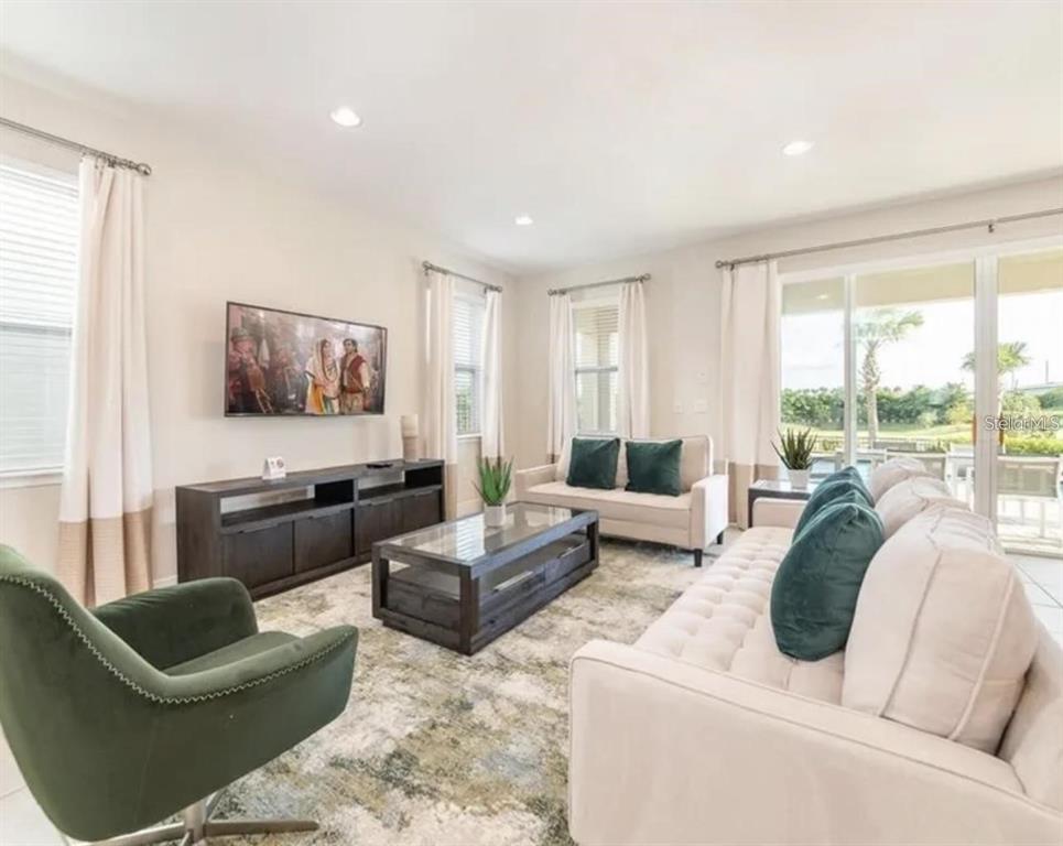 A living room features a beige sofa, green accent chair, coffee table, and television console — 7437 MARKER AVENUE, KISSIMMEE, FL