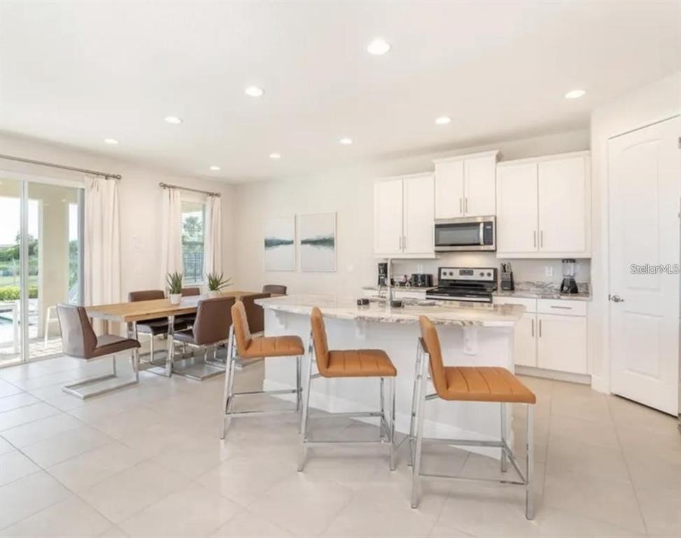 A bright kitchen with white cabinets, a marble-topped island, and an adjacent dining area — 7437 MARKER AVENUE, KISSIMMEE, FL