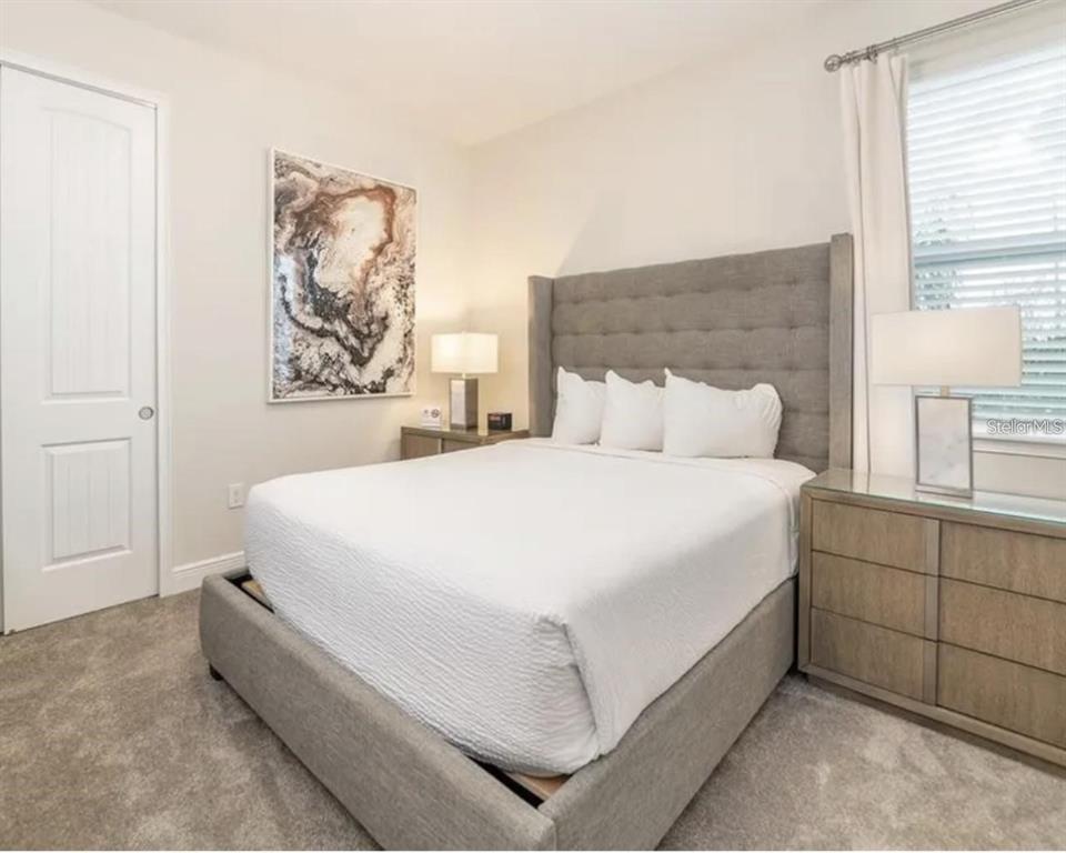 A bedroom features a gray upholstered bed, two nightstands with lamps, and abstract wall art — 7437 MARKER AVENUE, KISSIMMEE, FL
