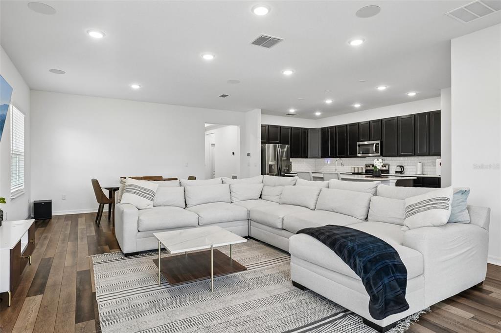 A spacious open-concept living room features a large sectional sofa, dining area, and kitchen — 11225 JUNE BRIAR LOOP, SAN ANTONIO, FL