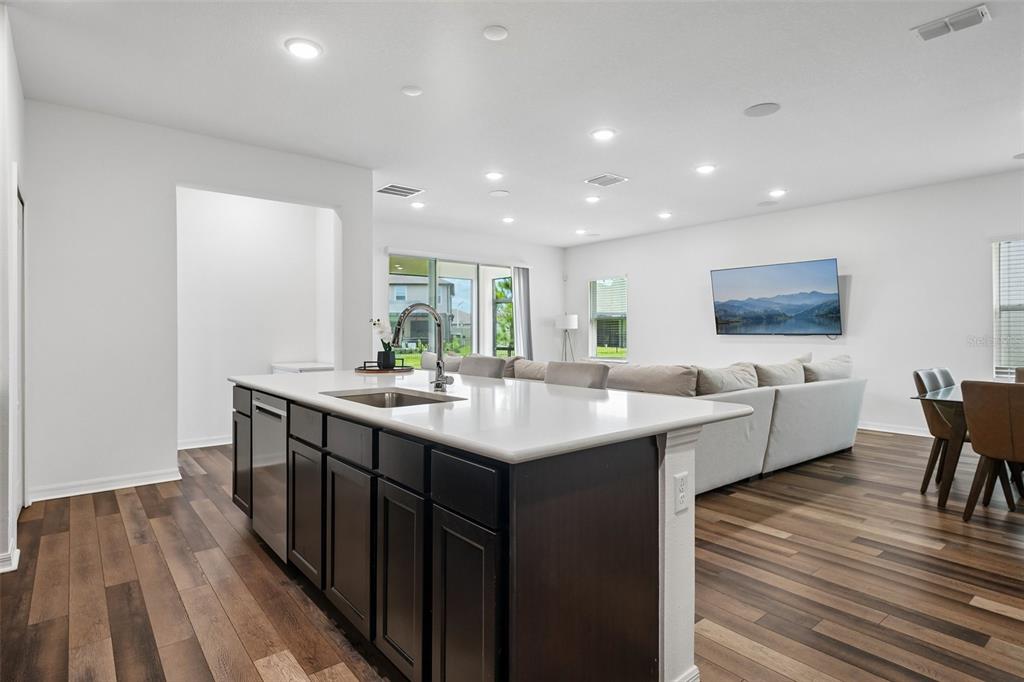 A modern kitchen island with dark cabinets and a white countertop faces a living area — 11225 JUNE BRIAR LOOP, SAN ANTONIO, FL