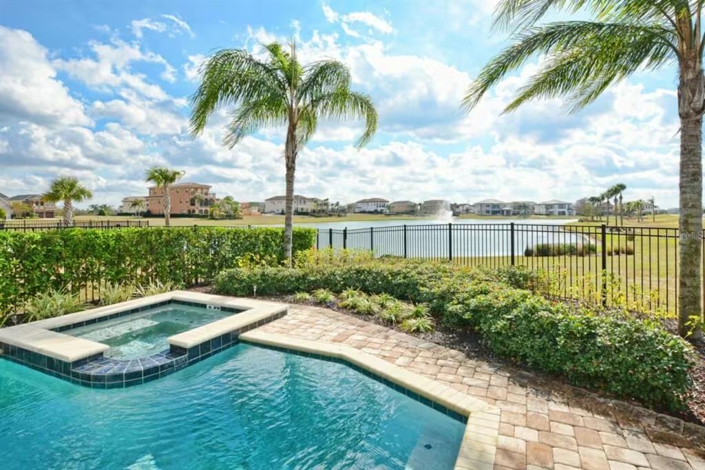 A backyard swimming pool and hot tub overlook a lake with houses in the distance — 7824 LOXAHATCHEE COURT, KISSIMMEE, FL