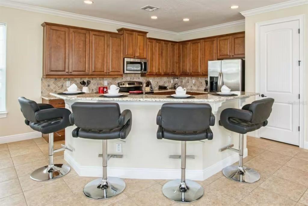 A kitchen features wood cabinets, granite countertops, and four black bar stools at a peninsula — 7824 LOXAHATCHEE COURT, KISSIMMEE, FL