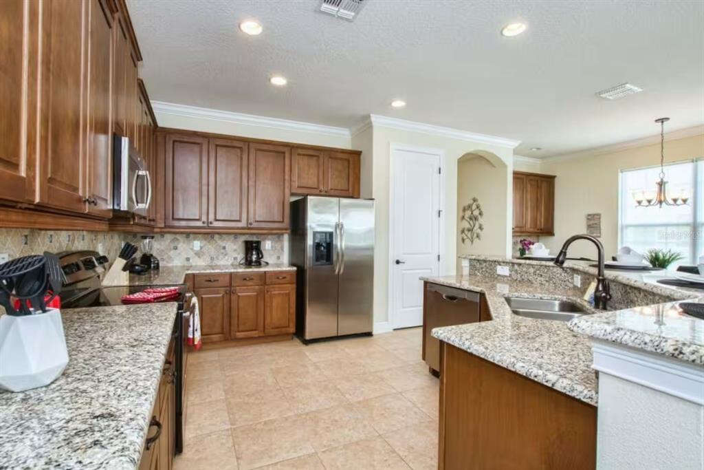 A kitchen features wood cabinets, granite countertops, stainless steel appliances, and tile flooring — 7824 LOXAHATCHEE COURT, KISSIMMEE, FL