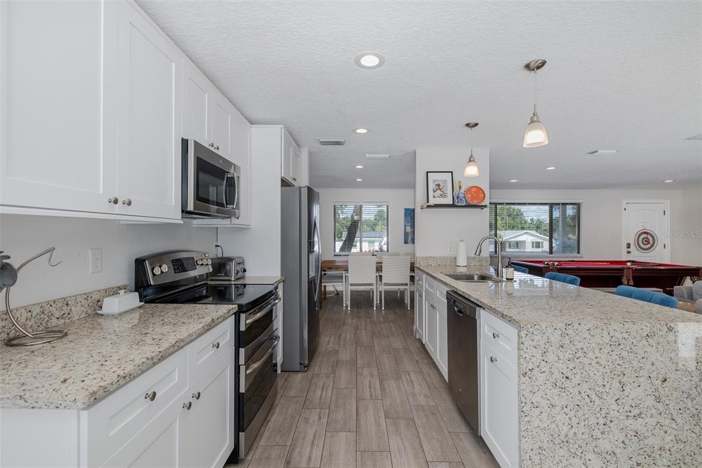 A kitchen with white cabinets, granite countertops, and stainless steel appliances overlooks a dining area — 2180 PHILIPPE PARKWAY, SAFETY HARBOR, FL