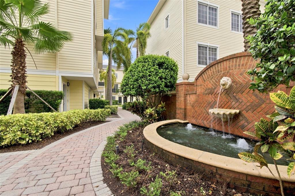 A brick fountain with a lion head spout sits beside a paved walkway between buildings — 9801 MEADOW FIELD CIRCLE, TAMPA, FL