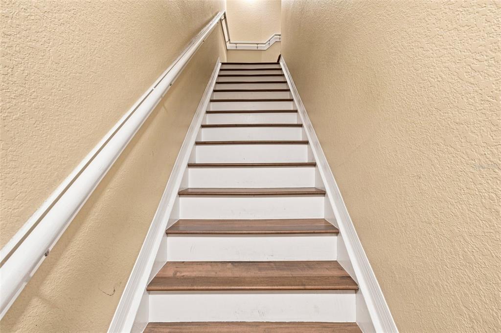 A straight staircase with wooden treads and white risers leads up between two beige walls — 9801 MEADOW FIELD CIRCLE, TAMPA, FL