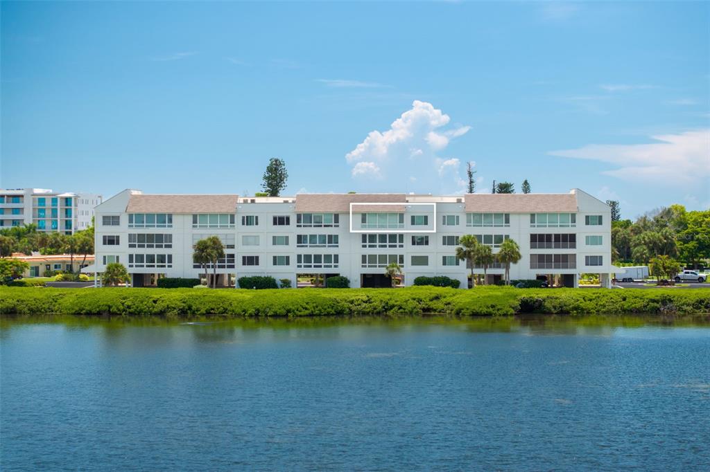 A multi-story residential building with white siding sits along a waterfront with green vegetation — 4800 GULF OF MEXICO DRIVE UNIT PH 3, LONGBOAT KEY, FL