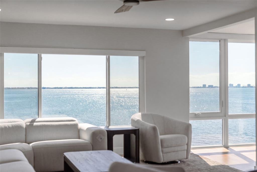 A living room with white furniture overlooks a large body of water through expansive windows — 4800 GULF OF MEXICO DRIVE UNIT PH 3, LONGBOAT KEY, FL