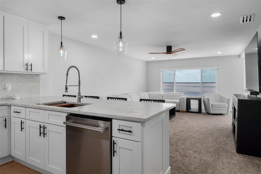 A modern kitchen with white cabinets and a stone island overlooks a carpeted living area — 4800 GULF OF MEXICO DRIVE UNIT PH 3, LONGBOAT KEY, FL
