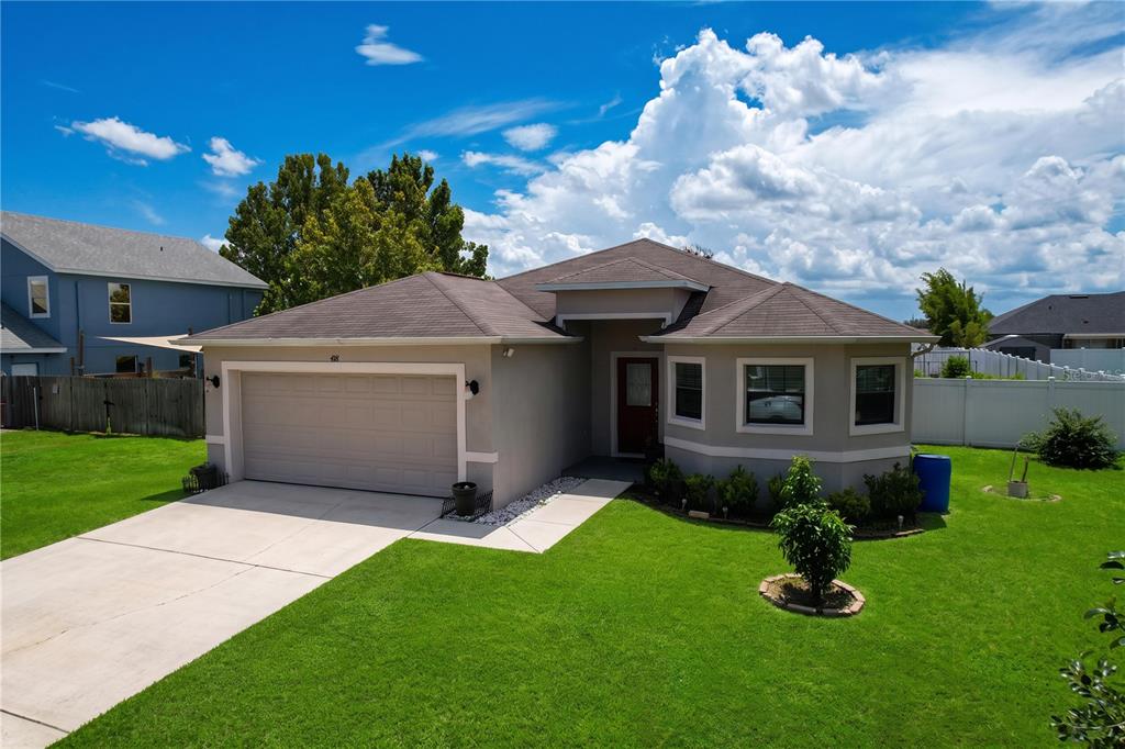 A single-story house with a beige exterior, a two-car garage, and a green lawn — 418 MAJESTIC GARDENS BLVD, WINTER HAVEN, FL