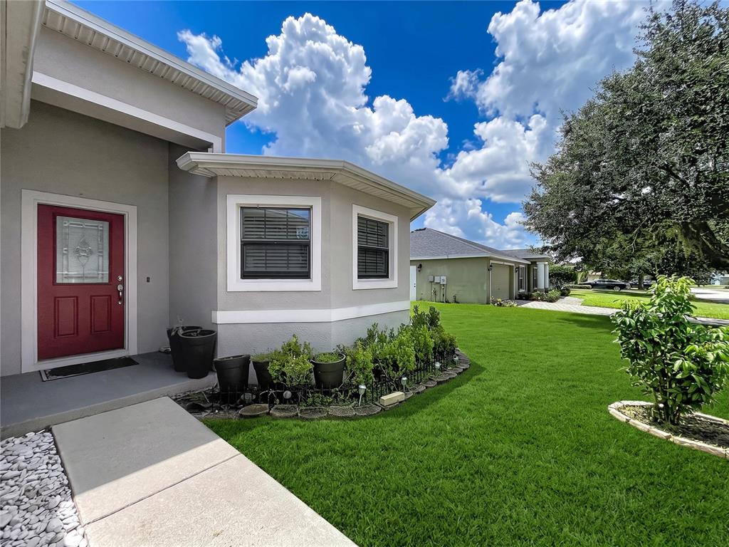 A gray house exterior features a red front door, a bay window, and a lawn — 418 MAJESTIC GARDENS BLVD, WINTER HAVEN, FL