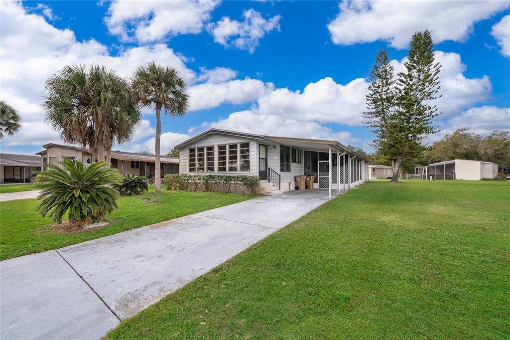 A light-colored mobile home with a concrete driveway and palm trees sits on a lawn — 2733 CRANMOOR DRIVE, KISSIMMEE, FL