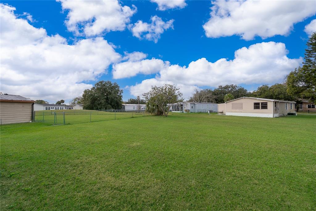 A large, grassy backyard features a chain-link fence and neighboring manufactured homes under a cloudy sky — 2733 CRANMOOR DRIVE, KISSIMMEE, FL
