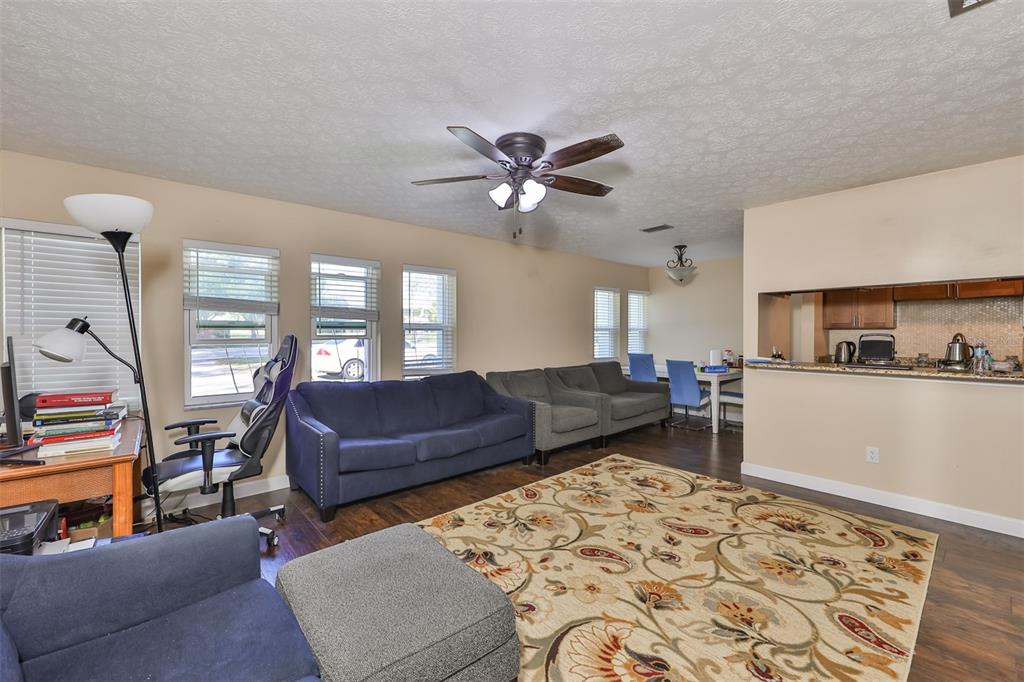 A living room features a blue sofa, gray armchairs, a patterned rug, and a kitchen pass-through — 103 N KINGSWAY ROAD, SEFFNER, FL