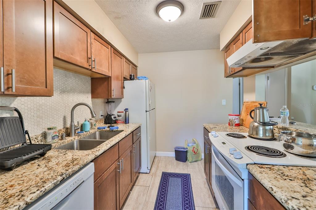 A galley kitchen features wood cabinets, granite countertops, a double sink, and white appliances — 103 N KINGSWAY ROAD, SEFFNER, FL