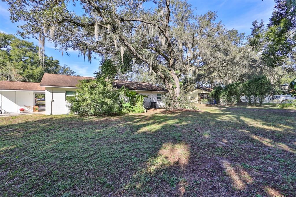A white house with a brown roof sits behind a large, tree-shaded grassy yard — 103 N KINGSWAY ROAD, SEFFNER, FL