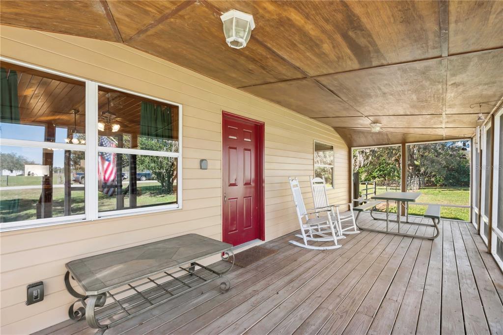 A covered wooden porch features a red front door, rocking chairs, and a picnic table — 2615 CR 762, WEBSTER, FL